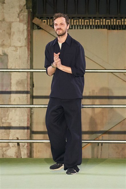 紺のシャツとパンツを着た男性が、ショーの最後に拍手へ応えている
